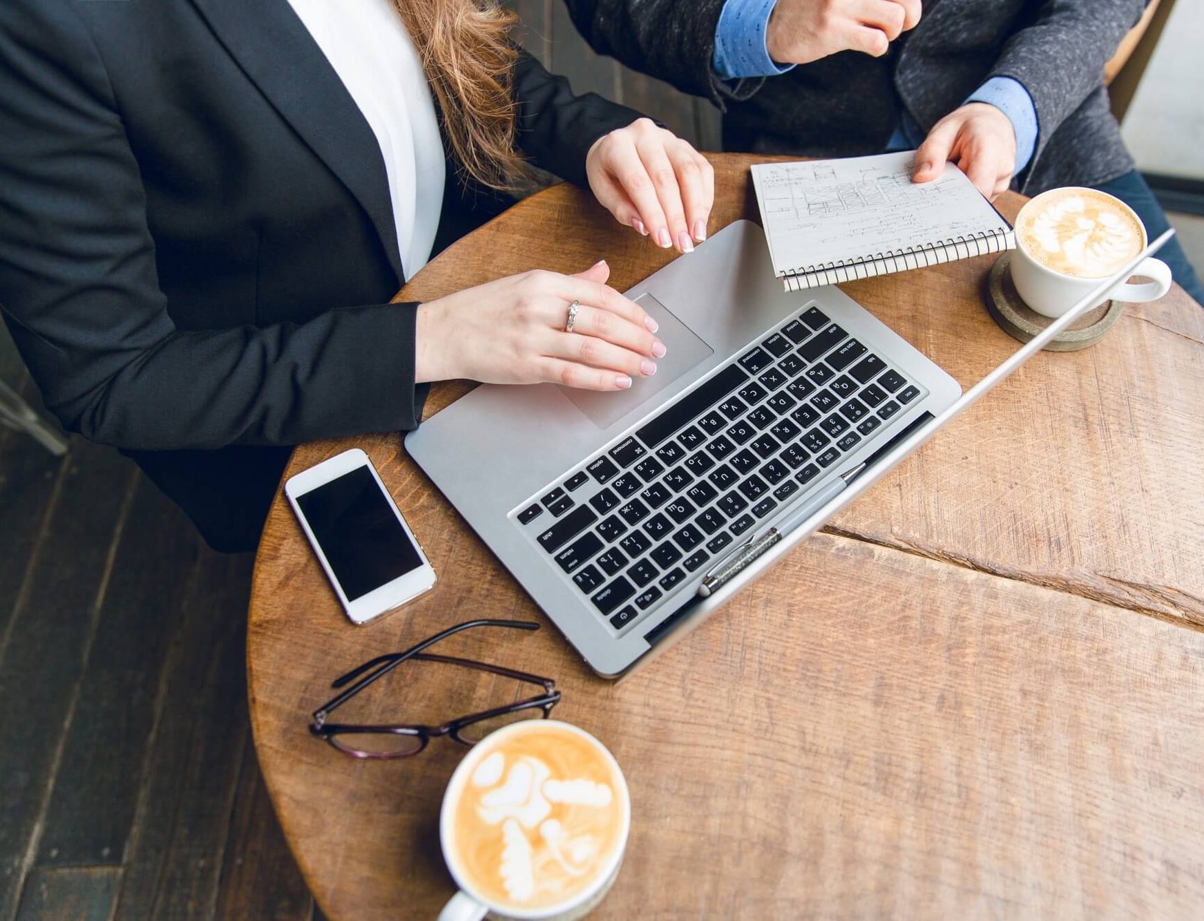 close-up-coffee-table-with-two-colleagues-sitting-holding-notebook-typing-laptop_197531-335 (1)